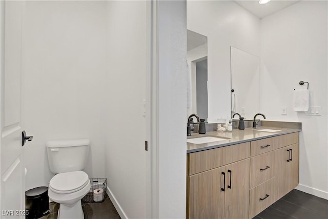 bathroom with a sink, double vanity, toilet, and baseboards