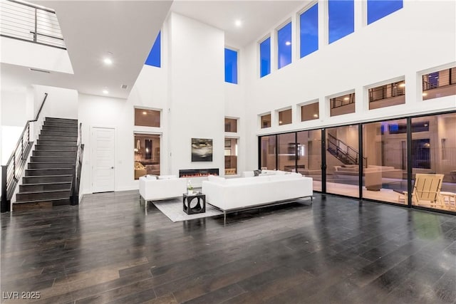 living room with a towering ceiling, stairway, and wood finished floors