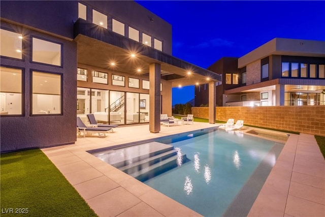 pool at night featuring stairway, fence, a fenced in pool, and a patio area