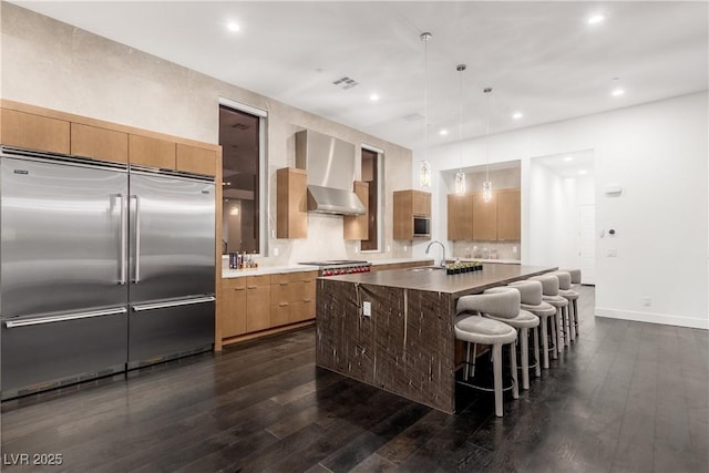 kitchen featuring wall chimney range hood, built in appliances, visible vents, and dark wood-style flooring
