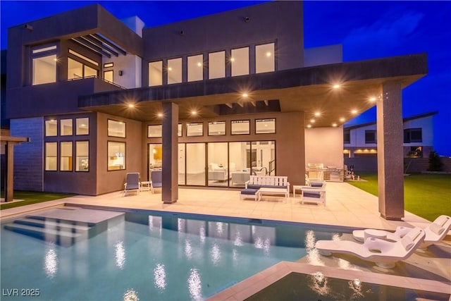 back of house at night featuring stucco siding, an outdoor pool, a patio, and an outdoor living space
