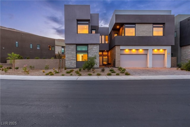 modern home with stone siding, fence, driveway, and an attached garage