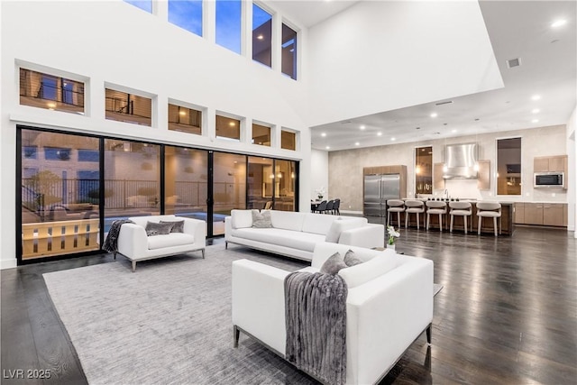 living room with dark wood finished floors, visible vents, recessed lighting, and a towering ceiling