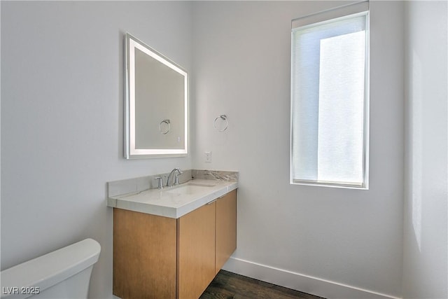 bathroom featuring baseboards, wood finished floors, toilet, and vanity
