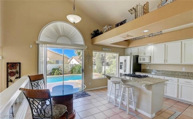 kitchen with stainless steel fridge, light tile patterned flooring, white microwave, white cabinetry, and a kitchen island