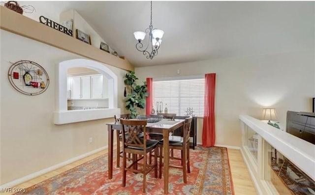 dining area with an inviting chandelier, lofted ceiling, baseboards, arched walkways, and wood finished floors