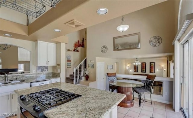 kitchen featuring light stone countertops, a sink, gas stove, a towering ceiling, and white cabinets