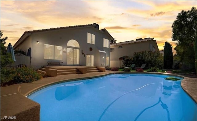 back of house featuring an outdoor pool, stucco siding, and a tiled roof