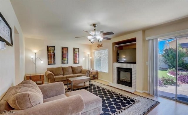 living room featuring ceiling fan, wood finished floors, a wealth of natural light, and a brick fireplace