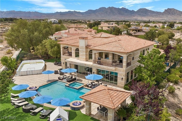 9301 Verlaine Ct, Las Vegas, NV 89145 - rear view of property featuring a balcony, a mountain view, a patio, a pool with connected hot tub, and stone siding