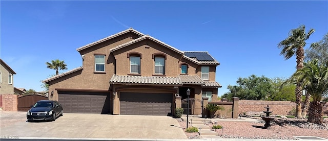 mediterranean / spanish house featuring a gate, roof mounted solar panels, concrete driveway, an attached garage, and fence