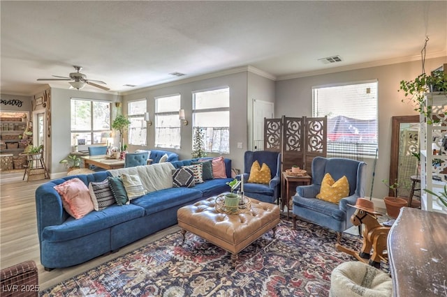 living area with wood finished floors, ceiling fan, baseboards, visible vents, and crown molding