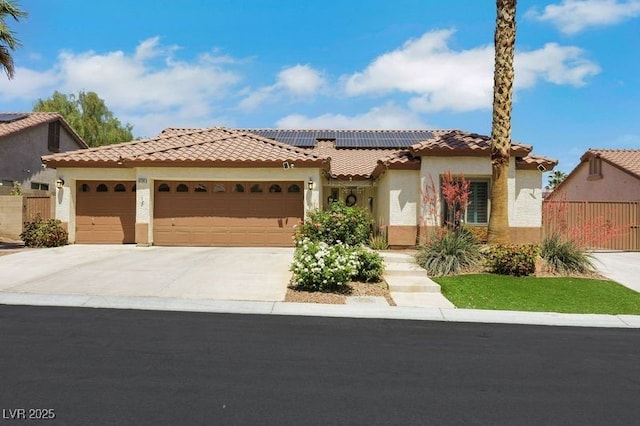 mediterranean / spanish home with stucco siding, a tiled roof, concrete driveway, solar panels, and an attached garage