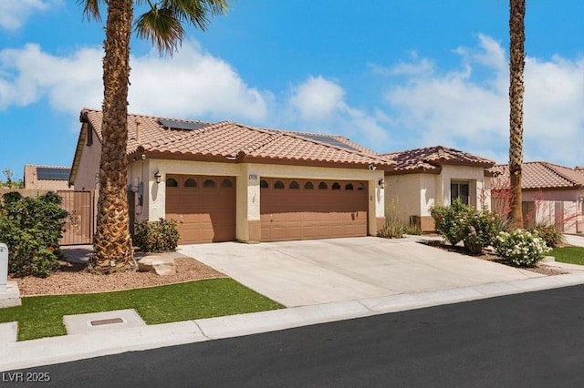 mediterranean / spanish-style home with stucco siding, a tiled roof, concrete driveway, solar panels, and an attached garage