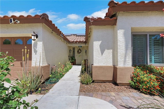 doorway to property featuring stucco siding, an attached garage, solar panels, and a tile roof