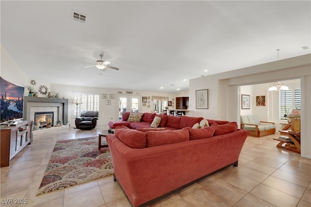 living area featuring light tile patterned floors, ceiling fan with notable chandelier, visible vents, and a healthy amount of sunlight