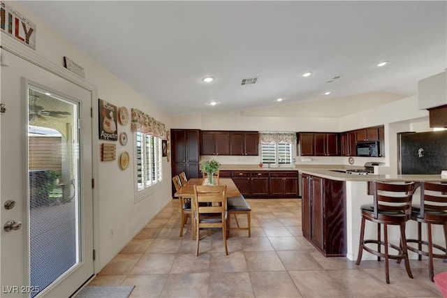 kitchen featuring refrigerator, light countertops, black microwave, visible vents, and lofted ceiling