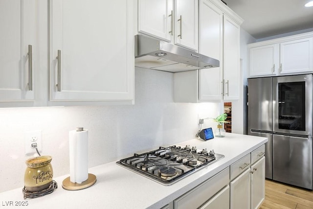kitchen featuring under cabinet range hood, appliances with stainless steel finishes, light countertops, white cabinets, and light wood-type flooring