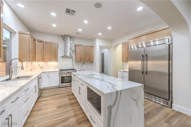2571 Red Springs Dr, Las Vegas, NV 89135 - kitchen featuring a sink, built in appliances, wall chimney exhaust hood, a kitchen island, and arched walkways