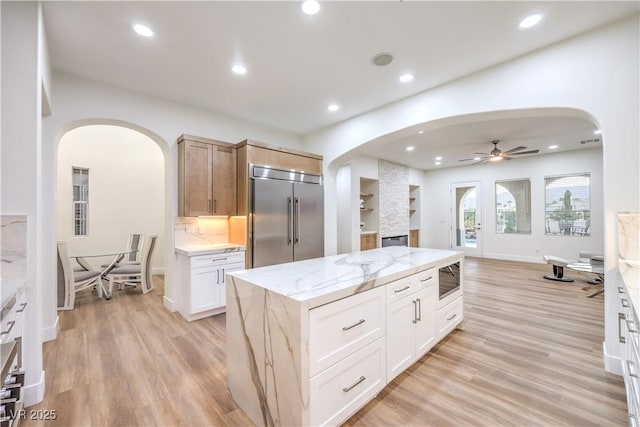 2571 Red Springs Dr, Las Vegas, NV 89135 - kitchen featuring stainless steel built in refrigerator, light wood-style flooring, ceiling fan, arched walkways, and light stone countertops