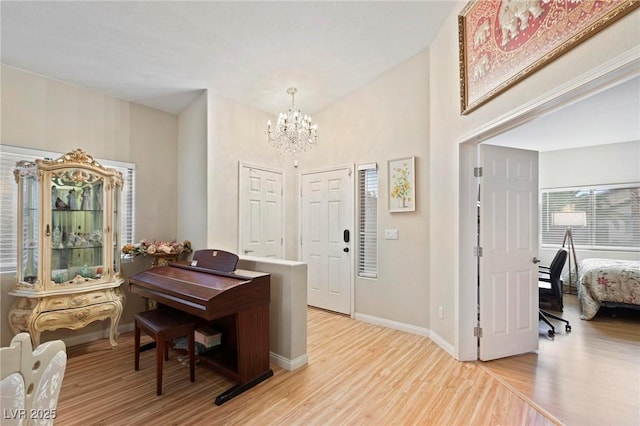 foyer featuring baseboards, a notable chandelier, a high ceiling, and light wood-style floors