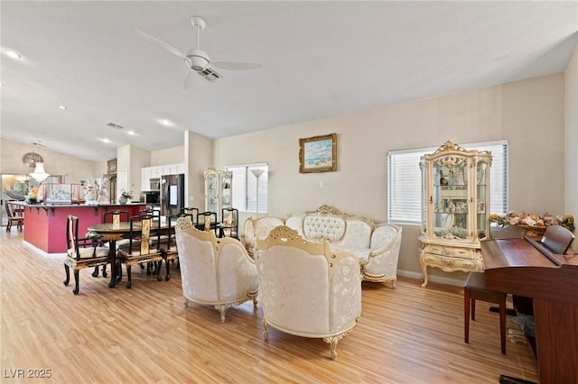 living room featuring vaulted ceiling, ceiling fan, light wood-type flooring, and visible vents
