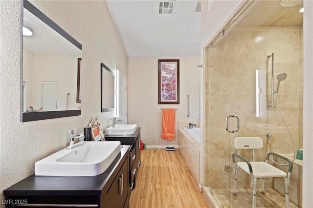 full bath with a sink, a stall shower, visible vents, and wood finished floors