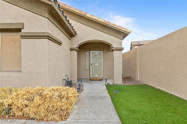 view of exterior entry with a tile roof, fence, and stucco siding