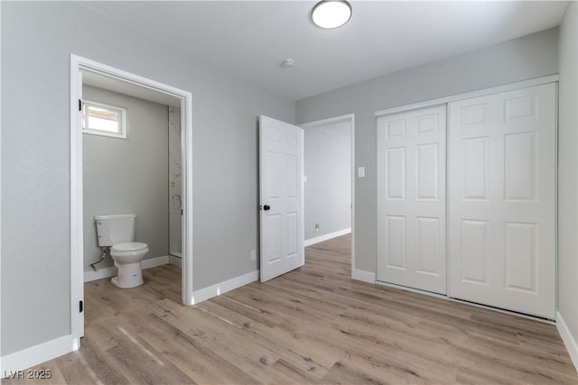 unfurnished bedroom featuring a closet, ensuite bath, baseboards, and light wood-style floors
