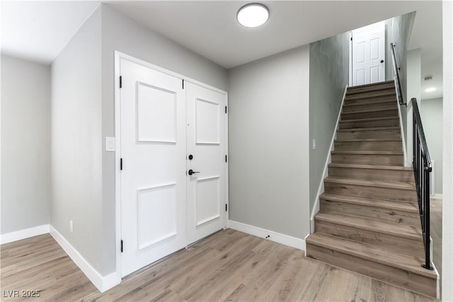 foyer entrance with baseboards, stairway, and light wood-style floors