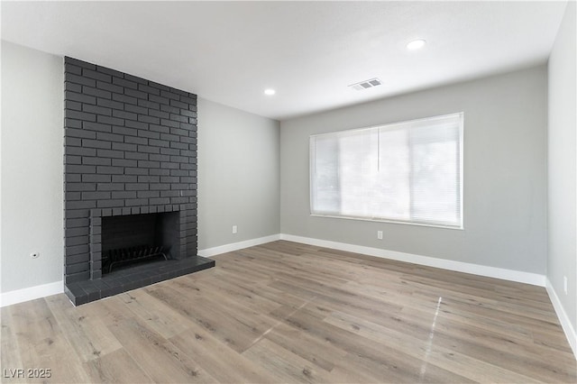unfurnished living room with wood finished floors, visible vents, and a brick fireplace