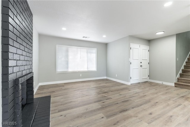 unfurnished living room featuring baseboards, visible vents, stairs, and a fireplace