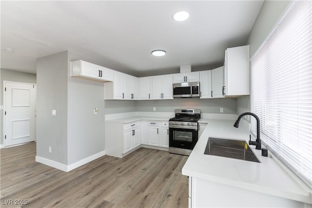 kitchen with a sink, light wood-type flooring, baseboards, light countertops, and appliances with stainless steel finishes