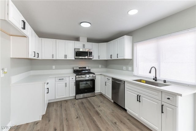 kitchen featuring white cabinets, light wood-type flooring, appliances with stainless steel finishes, and a sink