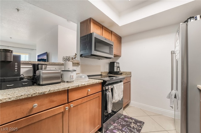 kitchen featuring brown cabinetry, baseboards, appliances with stainless steel finishes, and light tile patterned flooring
