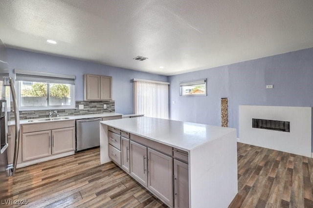 417 Wisteria Ave, Las Vegas, NV 89107 - kitchen with stainless steel dishwasher, wood finished floors, backsplash, light countertops, and a center island