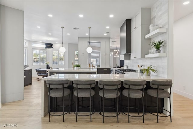 kitchen featuring open shelves, light countertops, wall chimney exhaust hood, a peninsula, and decorative backsplash