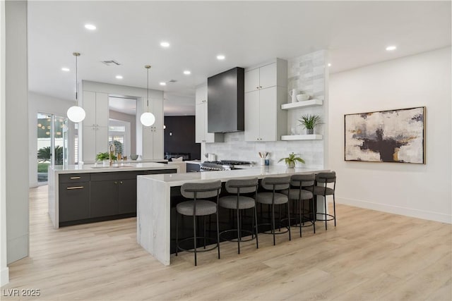 kitchen featuring open shelves, a sink, light countertops, wall chimney exhaust hood, and a peninsula