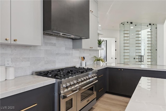 kitchen with decorative backsplash, white cabinetry, double oven range, and wall chimney exhaust hood
