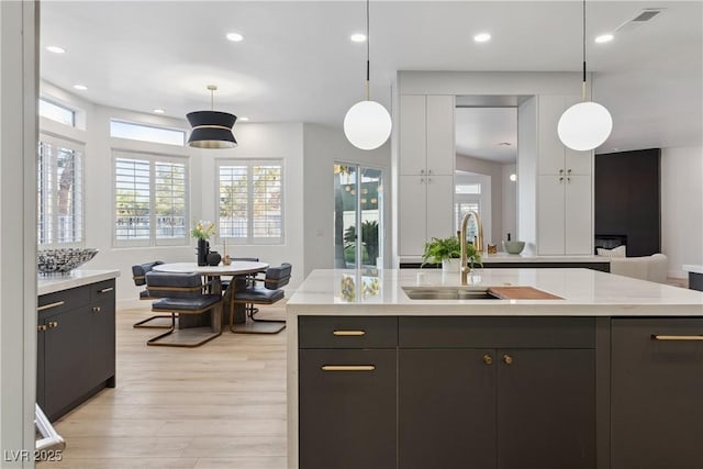 kitchen with open floor plan, light countertops, a sink, light wood-style flooring, and decorative light fixtures
