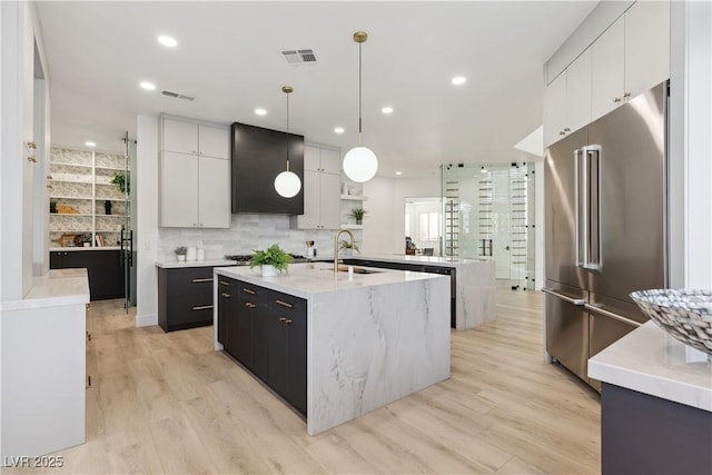 kitchen with visible vents, an island with sink, a sink, backsplash, and stainless steel appliances