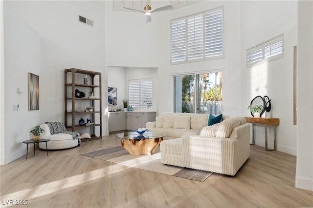 living room with baseboards, visible vents, light wood finished floors, and a towering ceiling