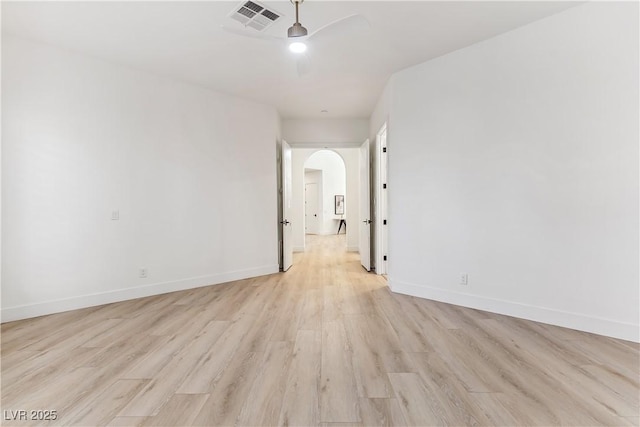 empty room with a ceiling fan, visible vents, arched walkways, baseboards, and light wood finished floors