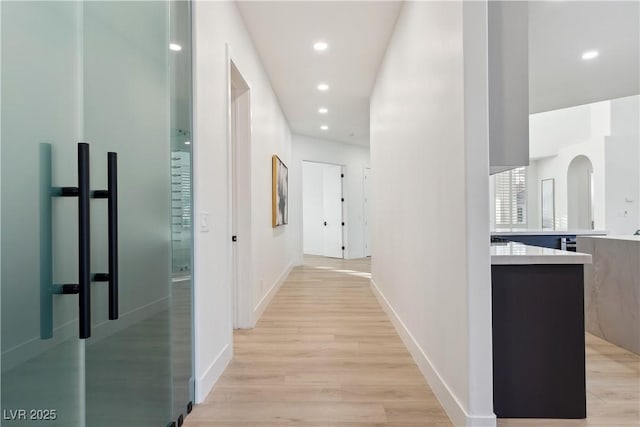 corridor featuring recessed lighting, baseboards, arched walkways, and light wood-style floors