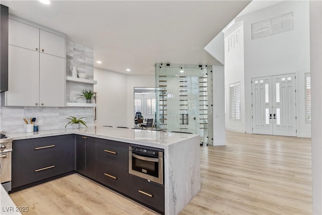 kitchen with appliances with stainless steel finishes, tasteful backsplash, open shelves, a peninsula, and light wood finished floors