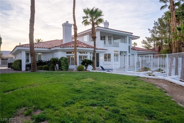 back of property with a tiled roof, a chimney, fence, a yard, and stucco siding