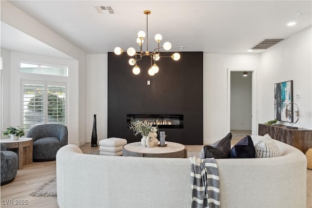 living room featuring a glass covered fireplace, baseboards, light wood finished floors, and visible vents