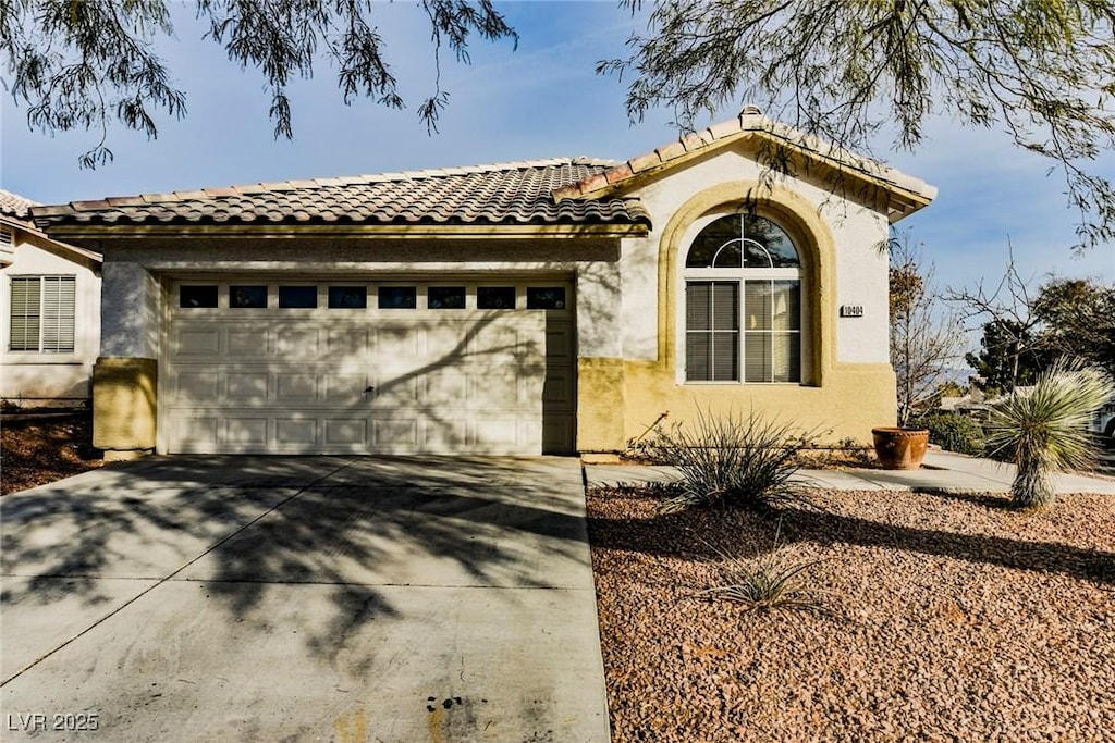 mediterranean / spanish-style home with a tile roof, driveway, an attached garage, and stucco siding