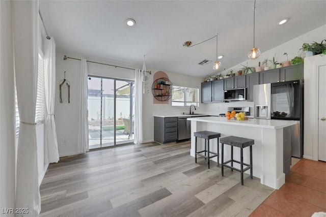 kitchen with stainless steel appliances, light countertops, a kitchen bar, a sink, and gray cabinetry