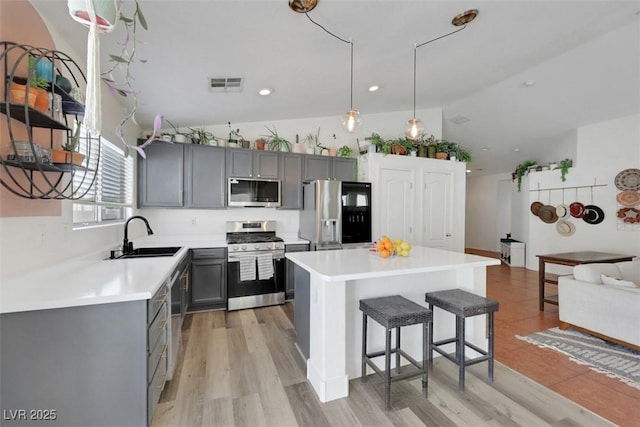 kitchen with gray cabinets, stainless steel appliances, a kitchen bar, a sink, and visible vents